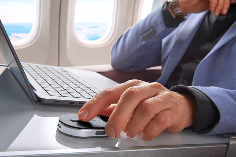 Mann in einem Flugzeug nutzt eine mobile Mini-Maus auf einem Tisch.