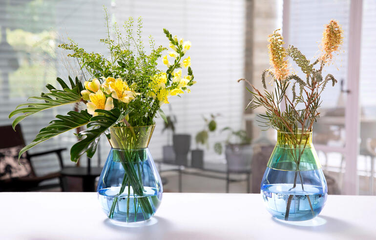 Zwei Twotone Vasen mit bunten Blumen auf einem Tisch in einem hellen Raum.