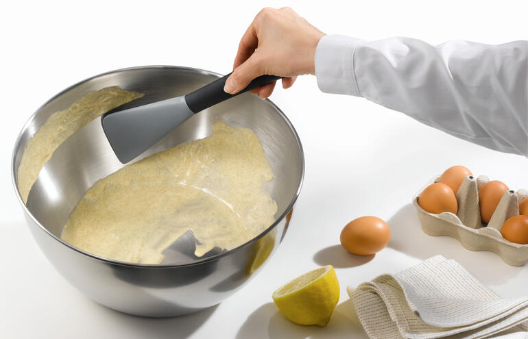 Flexibler Silikonspatel, der Teig aus einer großen Schüssel schöpft.