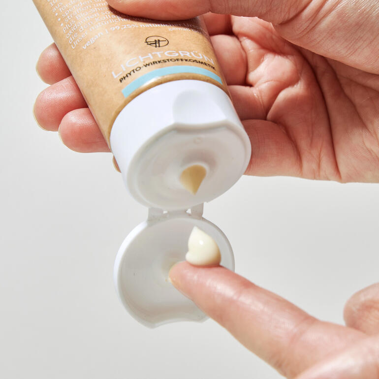 Hand drückt eine Naturkosmetik-Tube aus, mit einem kleinen Klecks Creme auf dem Finger.