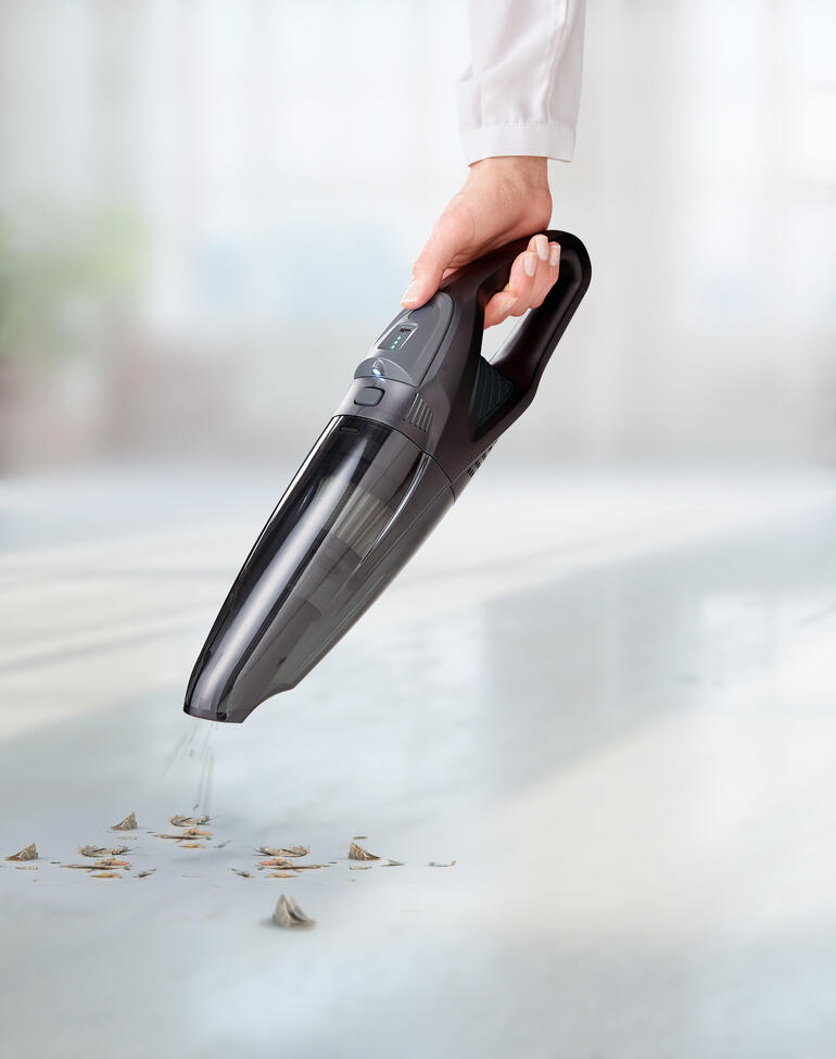 Person hält einen Akku-Handsauger über den Boden, um Schmutz zu beseitigen.