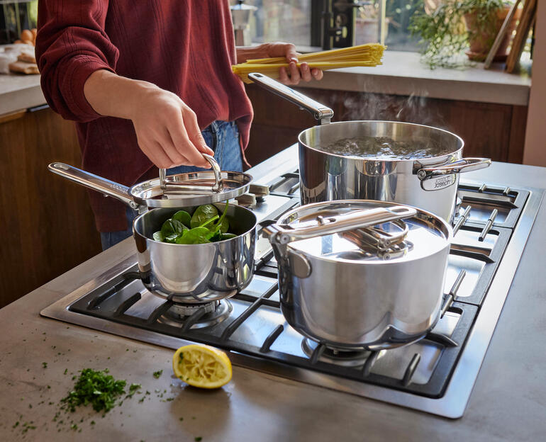 Kochgeschirr-Set mit Klappgriff, eine Pfanne und zwei Töpfe mit Gemüse auf dem Herd.