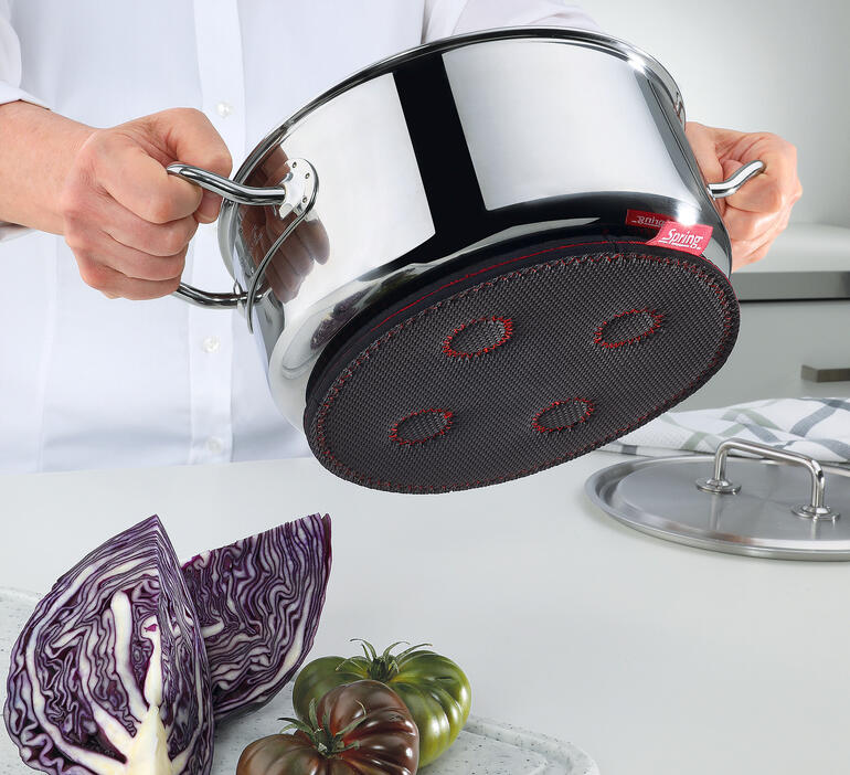 Hand hält einen magnetischen Untersetzer unter einen Kochtopf.