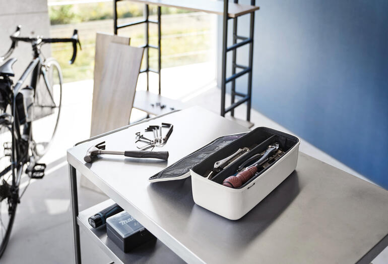 Tool-Box auf einem Tisch mit Werkzeugen im Hintergrund.