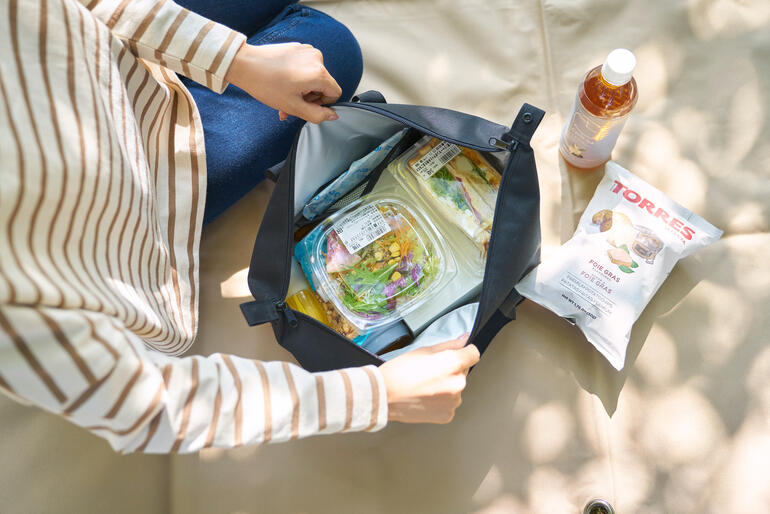 Frau öffnet eine Vario-Kühltasche und zeigt frische Lebensmittel im Inneren.