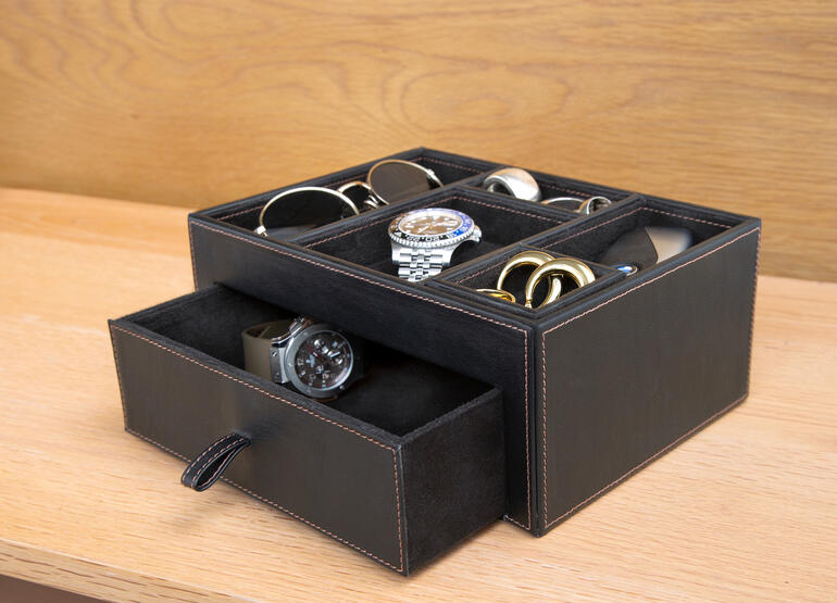 Schwarze Lederablage mit verschiedenen Accessoires wie Uhren und Brillen.