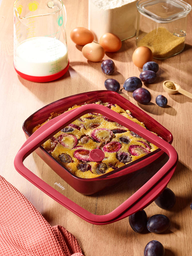 Rote Ofenform mit Deckel, gefüllt mit einem Obstgericht auf einem Tisch.