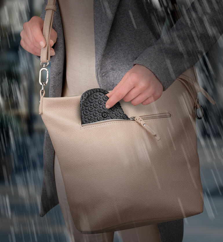 Person nimmt einen schwarzen Silikon-Schuhüberzieher aus ihrer Handtasche im Regen.