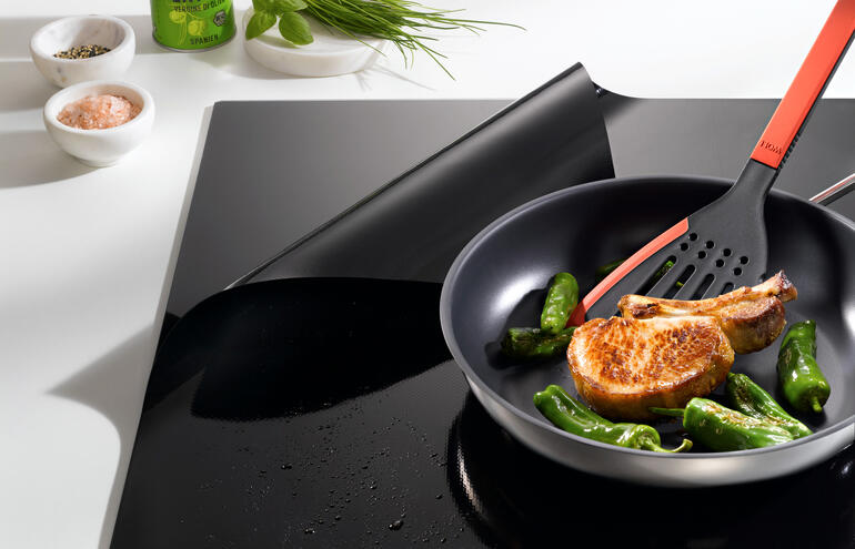 Pfanne mit Zucchini und einem Kotelett auf einem Induktions-Kochfeldschutz