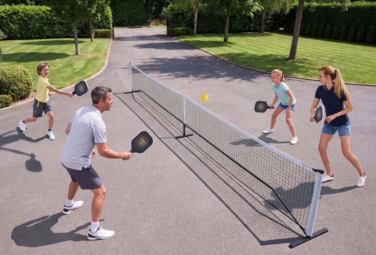 Familie spielt Pickleball im Freien, mit Netz und Bällen.