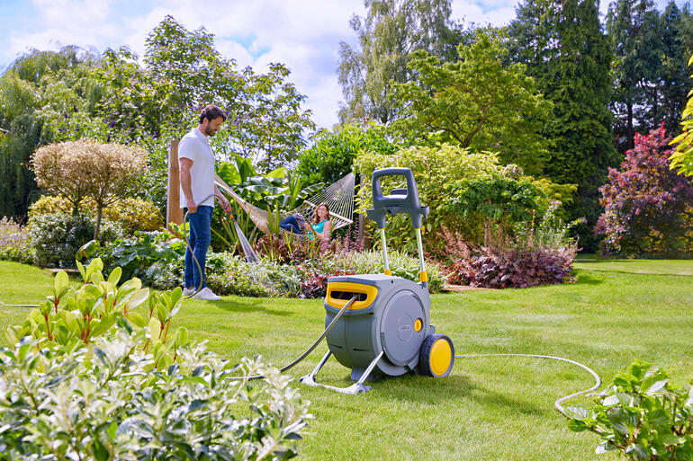 Mann gießt Wasser mit einem Schlauch aus einem geschlossenen Schlauchwagen