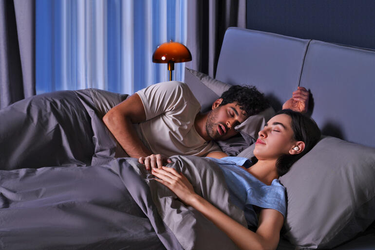 Paar schläft im Bett, Ohrhörer-/Schlafstöpsel auf dem Kopfkissen.