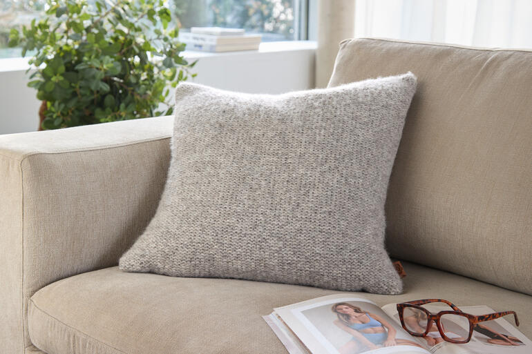 Graues Alpaka-Leinen-Kissen auf einem hellen Sofa mit Brille und Magazin.