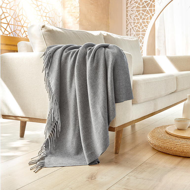 Handgewebte Kaschmir-Kuscheldecke über einer hellen Couch drapiert.