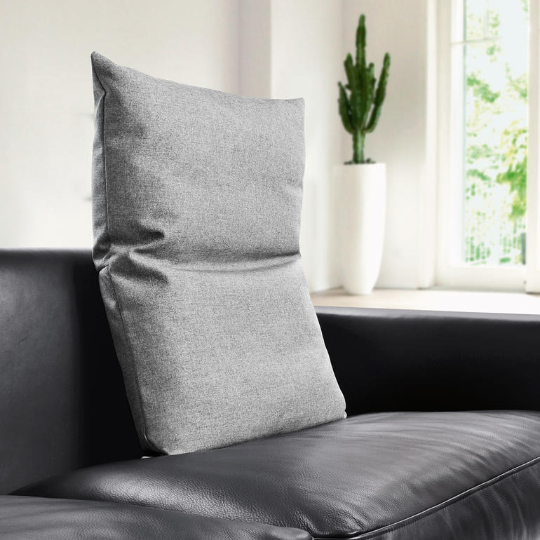 Hellgraues Rückenkissen auf einer schwarzen Couch.
