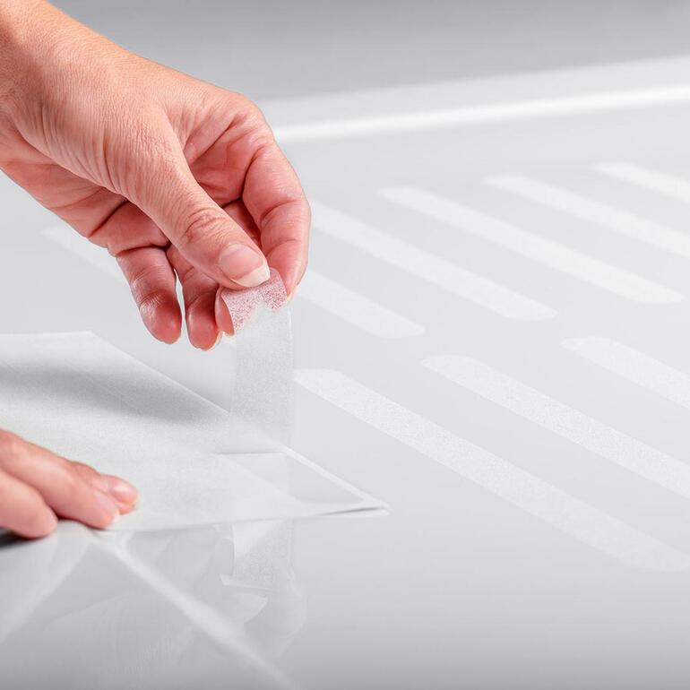 Satho® Rutschschutz-Streifen, 10er-Set Eine Hand klebt einen Rutschschutz-Streifen auf einen Duschboden
