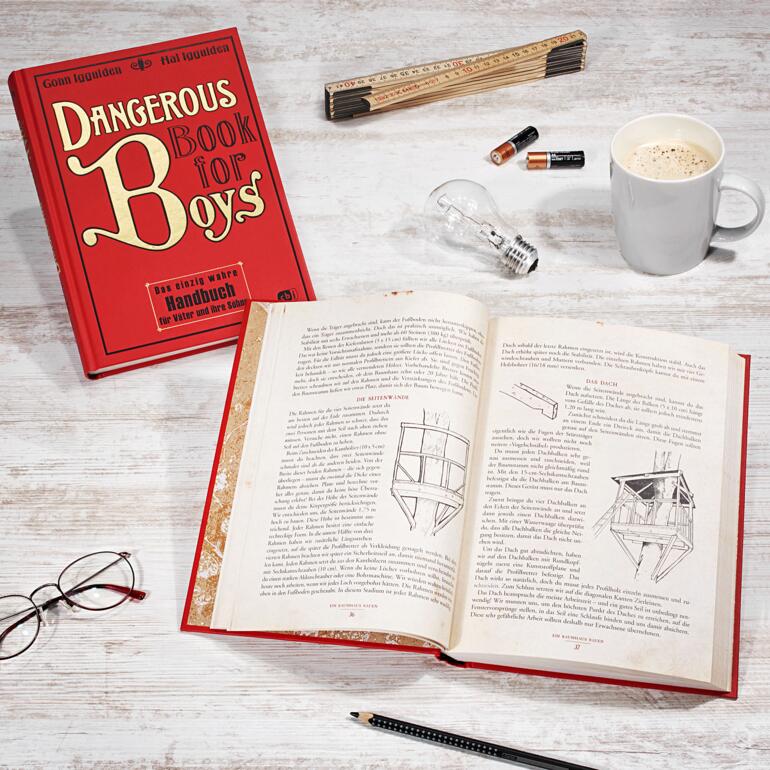 Buch 'Dangerous Book for Boys' auf einem Tisch, offen mit einer Tasse Kaffee.