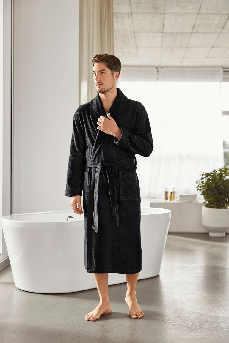 Mann in einem schwarzen Bademantel steht in einem modernen Badezimmer
