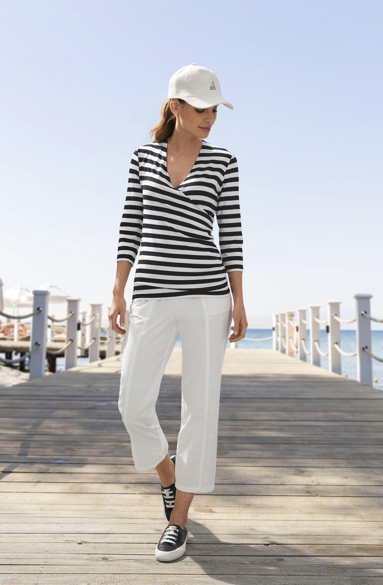 Frau in gestreifter Bluse und weißen Hosen, am Strand.