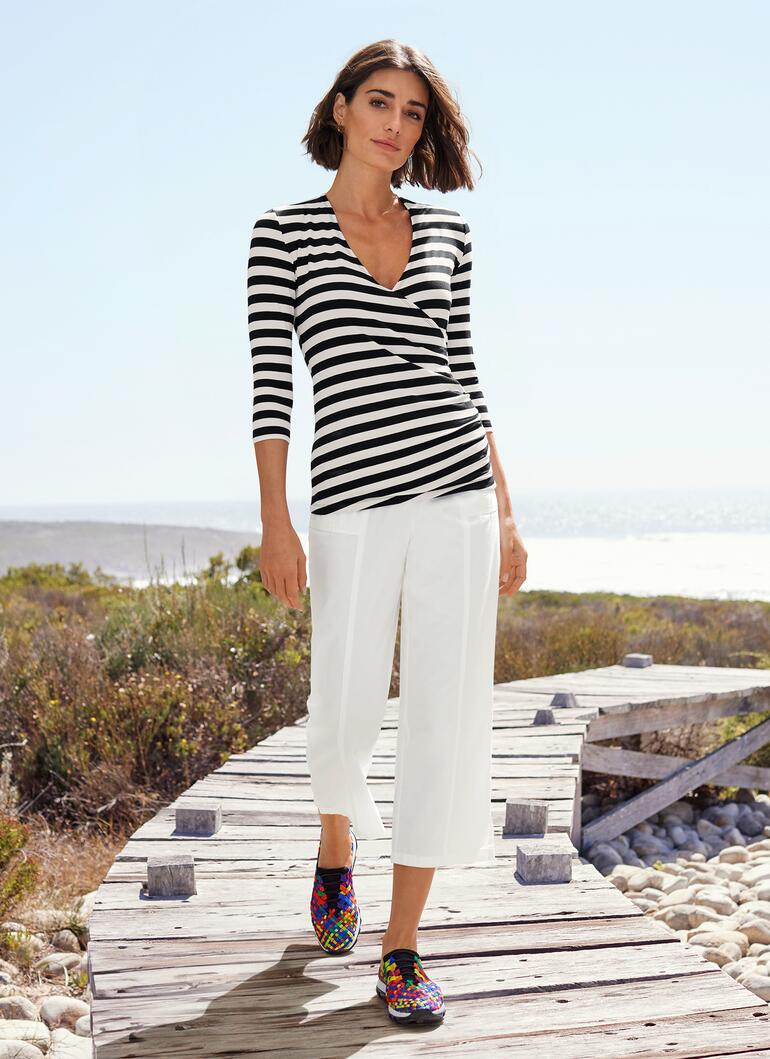 Frau in gestreifter Bluse und weißer Hose, auf Holzsteg.