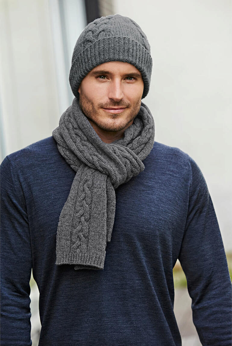 Mann in grauer Zopfstrick-Mütze und -Schal, trägt einen blauen Pullover.