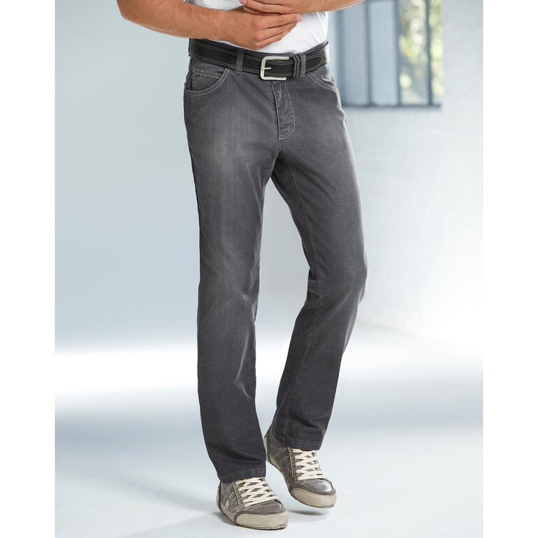 Mann in grauen Denim-Jeans und T-Shirt steht vor einem Fenster.