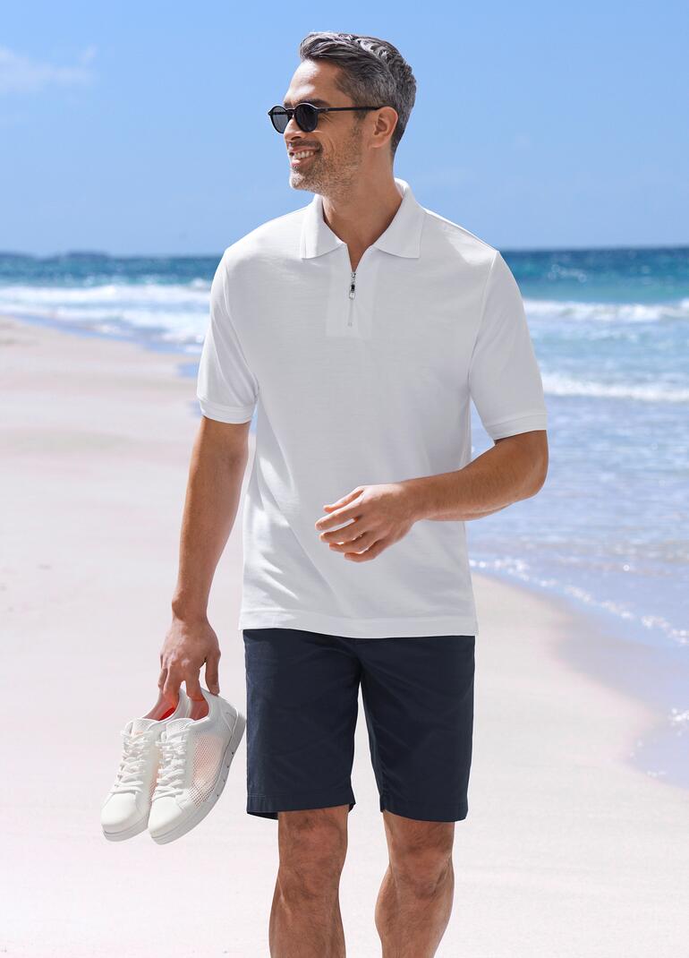 Weiss Mann in weißem Poloshirt und schwarzer Shorts am Strand.