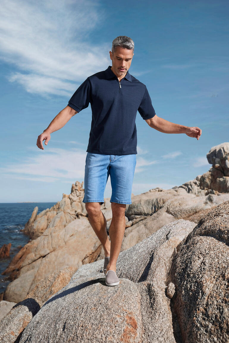 Mann trägt navy Coolmax-Kurzarm-Polo und steht auf Felsen am Meer.