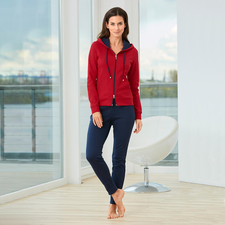Frau in rotem Pima-Cotton Homesuit und blauen Hosen steht in hellem Raum