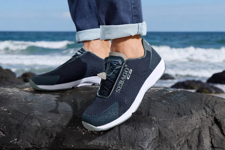 Sebago Herren-Wet-Sneakers in marineblau, getragen an einem Strand mit Wellen im Hintergrund.