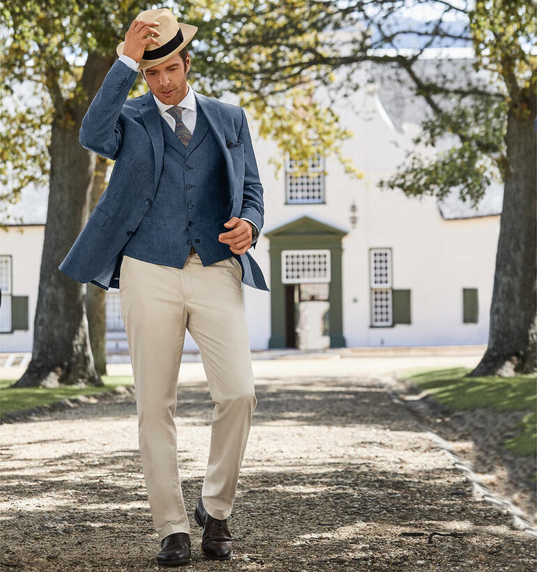 Mann mit Hut in einem eleganten Anzug und Paisley-Krawatte auf einem Weg.