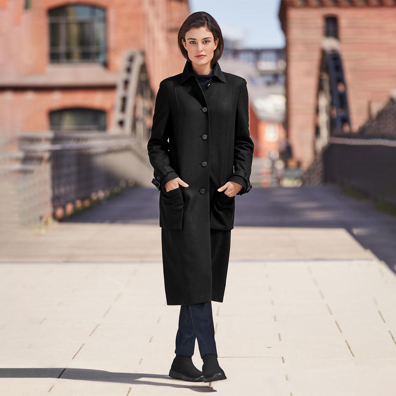 Frau in schwarzem Mantel mit Strickstiefeln auf einer Brücke.