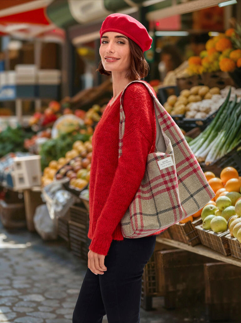Sac cabas à tartan BAZAR Atelier Sablon Frau trägt rote Baumwoll-Baskenmütze und einen roten Pullover, steht auf einem Markt.