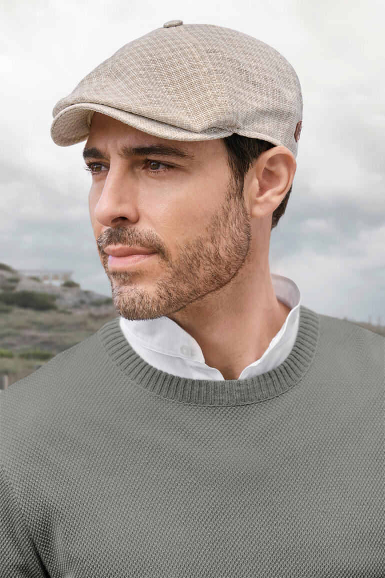 Mann trägt helle Schiebermütze mit einem grauen Pullover