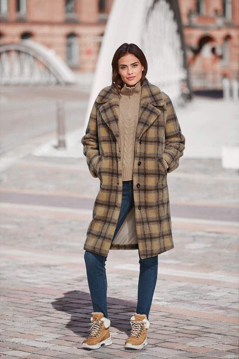 Frau in kariertem Teddy-Bär-Mantel mit Sneakern im Freien