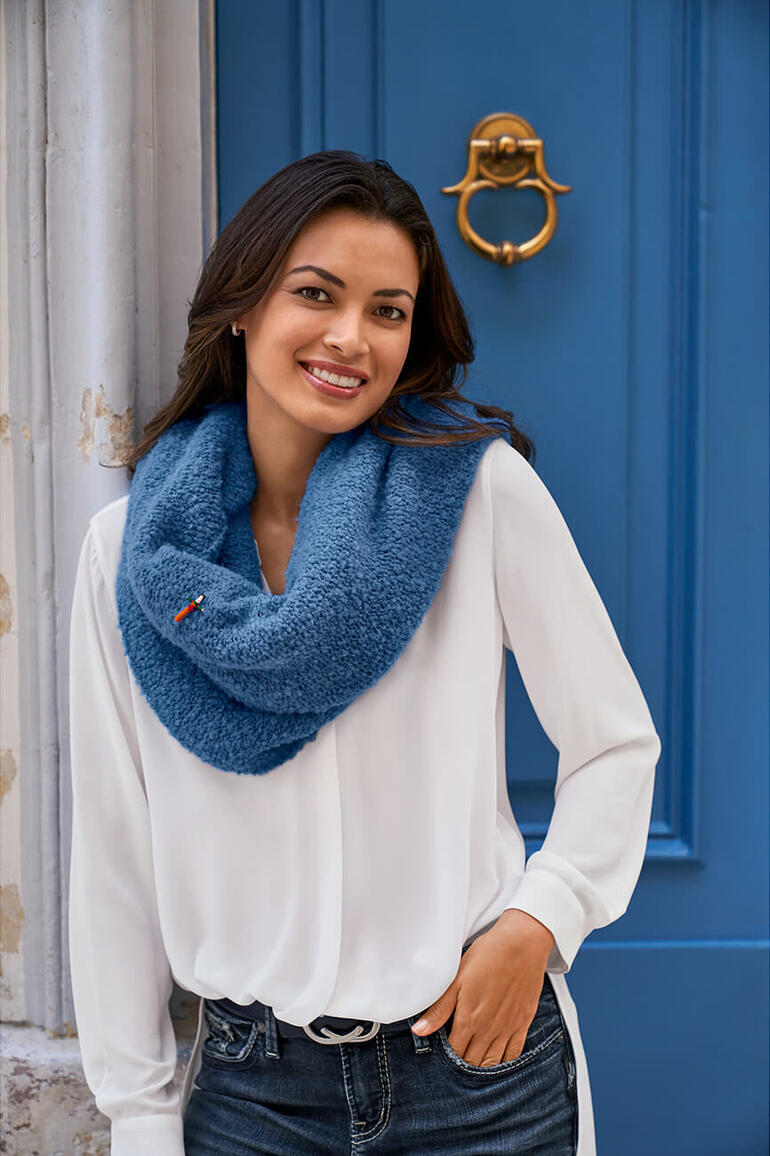 Frau trägt weißen Bluse mit blauem Bouclé-Poncho vor einer blauen Wand