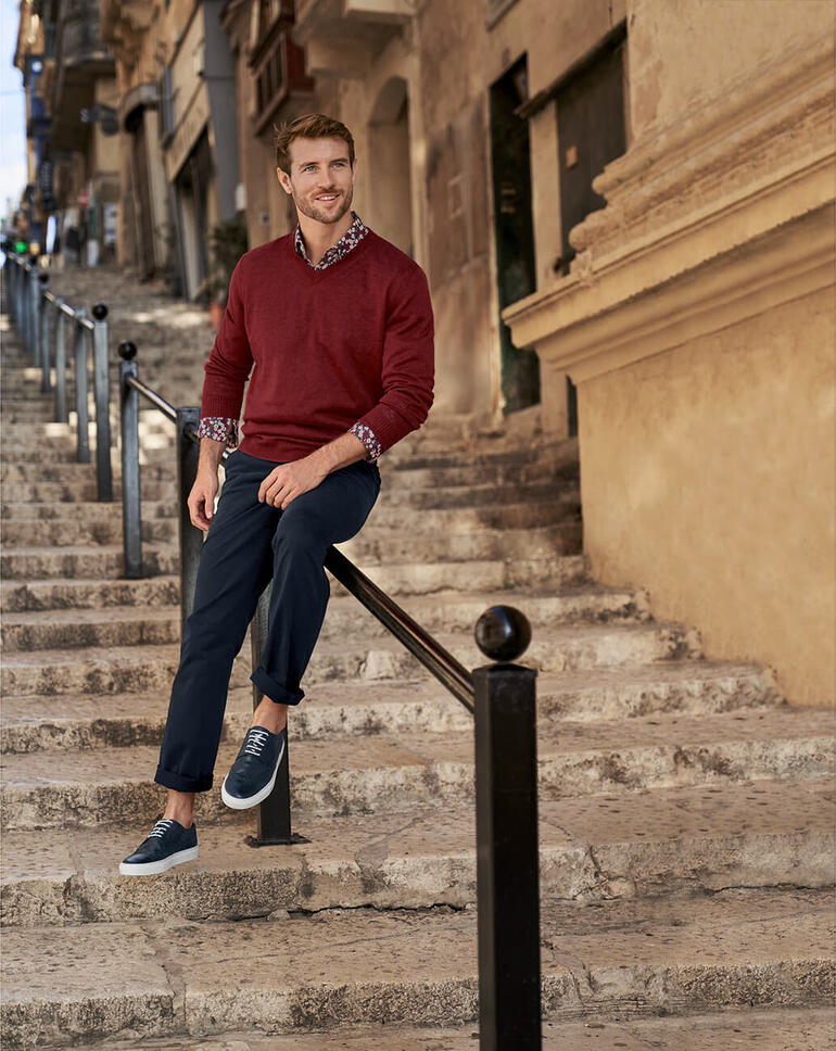 Mann in rot meliertem Leinenpullover sitzt auf Steintreppen in einer Stadt.