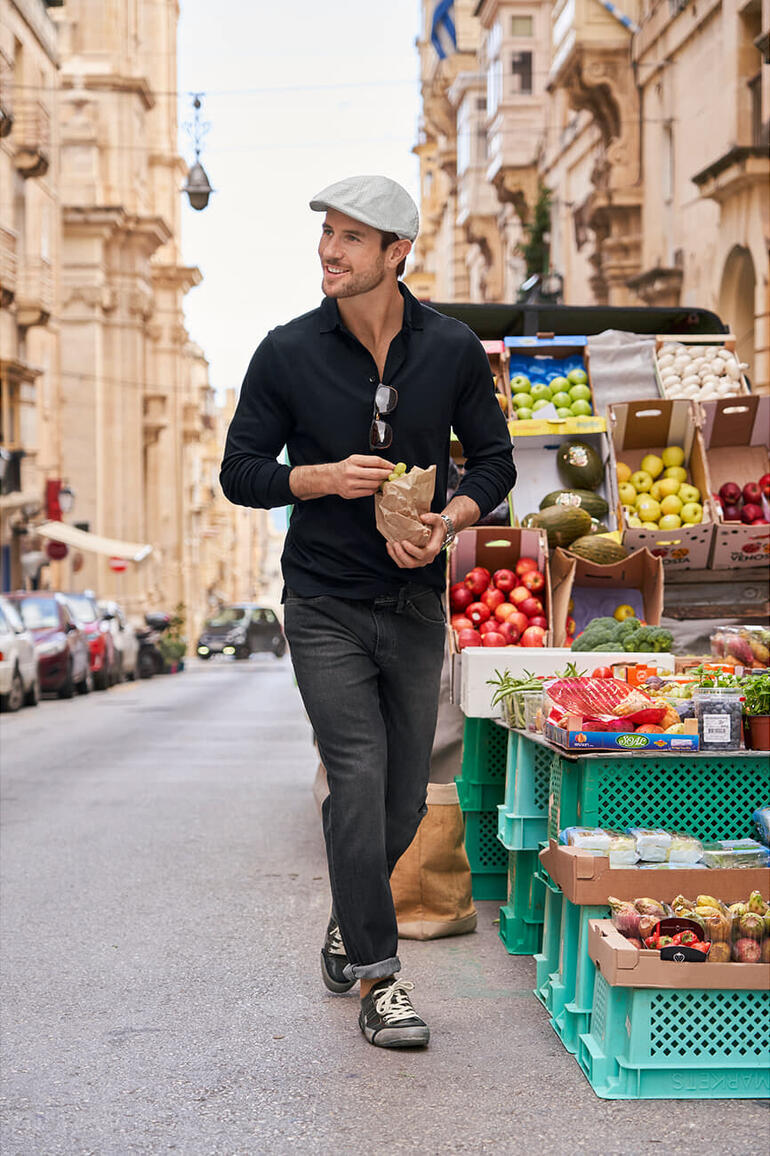Mann mit Bailey of Hollywood Seersucker-Schiebermütze auf Straßenmarkt, hält Tüte mit Essen.