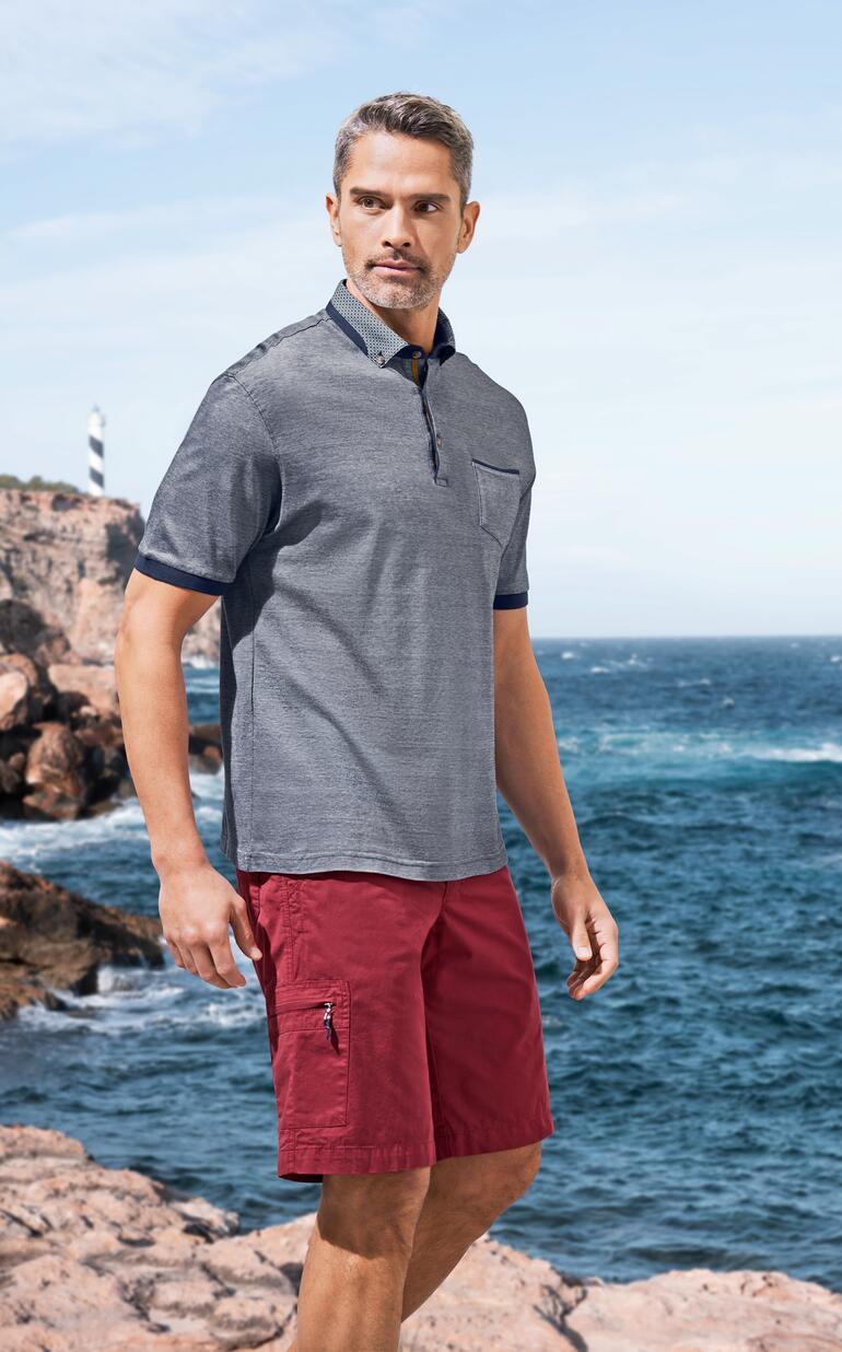 Mann trägt Poloshirt und Bermudas in rot, am Strand.