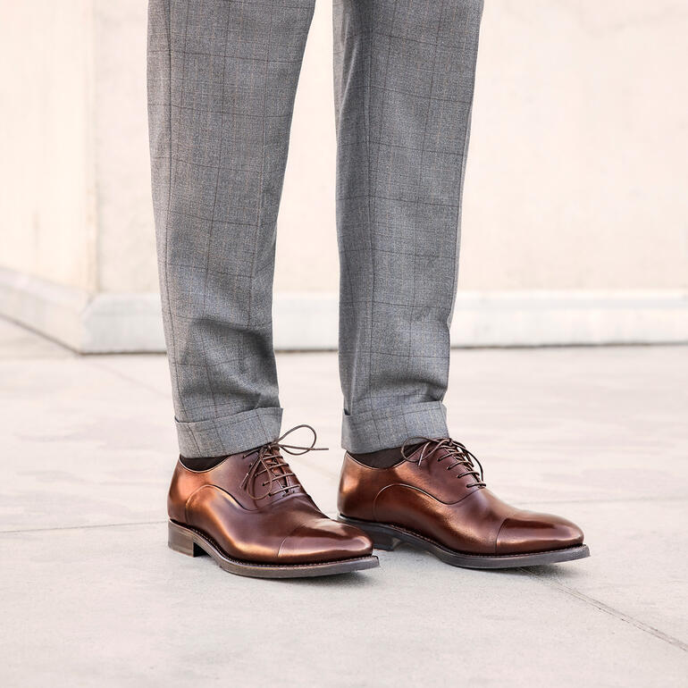 Mann in grauen Hosen und braunen Cordwainer Business-Schuhen im Stehen mit offenem Schuhkopf.