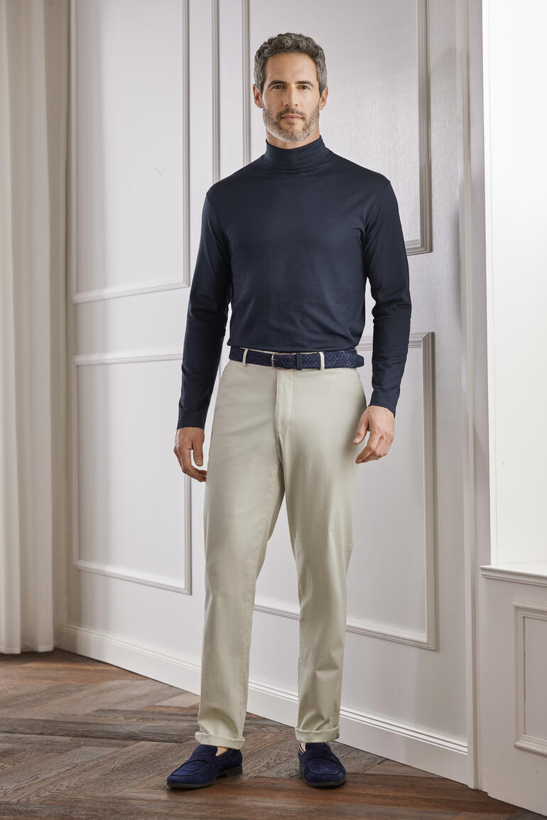 Creme Mann im dunklen Sunspel Unterzieh-Rolli und heller Hose in einem eleganten Raum.