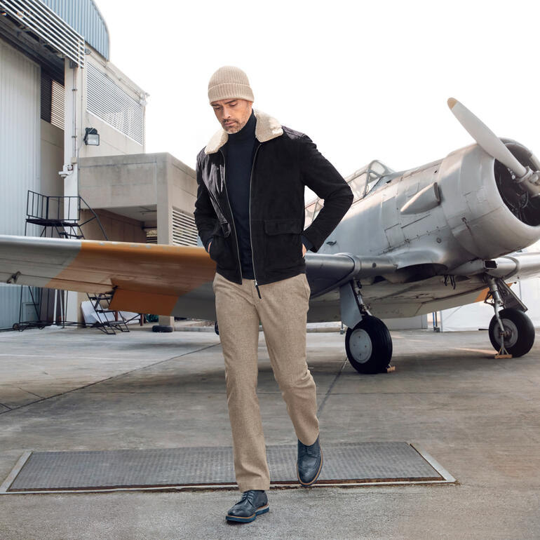 Mann in modischer Feinloden-Tuchhose vor einem Flugzeug