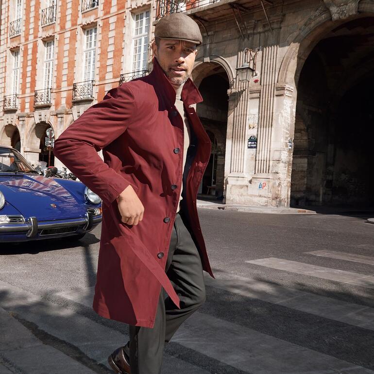 Mann in rotem Leicht-Trenchcoat läuft über eine Straße vor historischen Gebäuden.