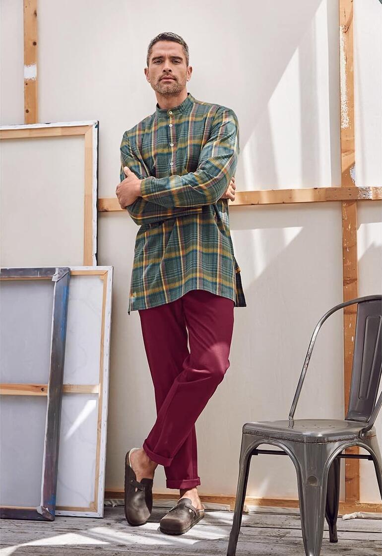 Mann in bordeauxfarbenen Chinos und kariertem Hemd, stehend.