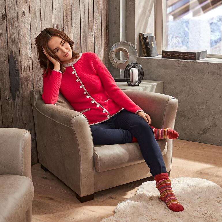 Frau in rotem Herzallerliebst-Janker sitzt in einem Sessel und schaut nachdenklich.