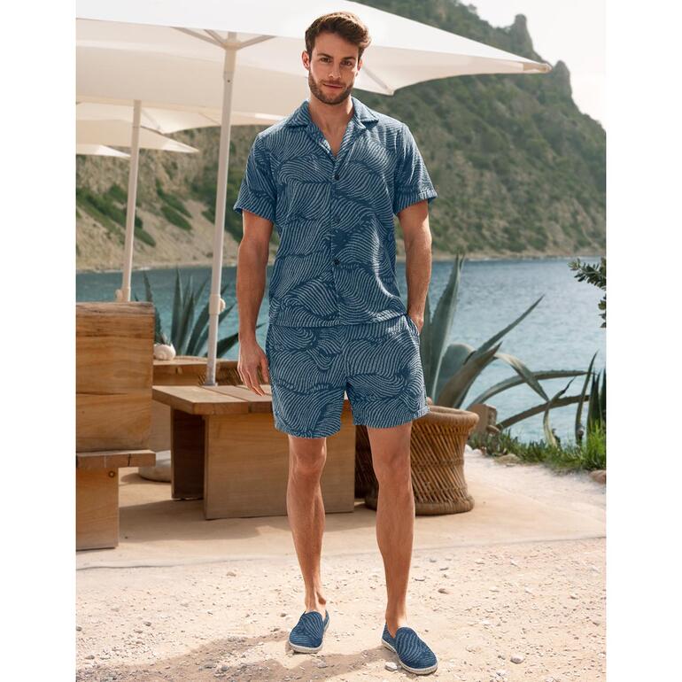 Mann in gestreiftem Terry-Shirt und Shorts steht am Strand