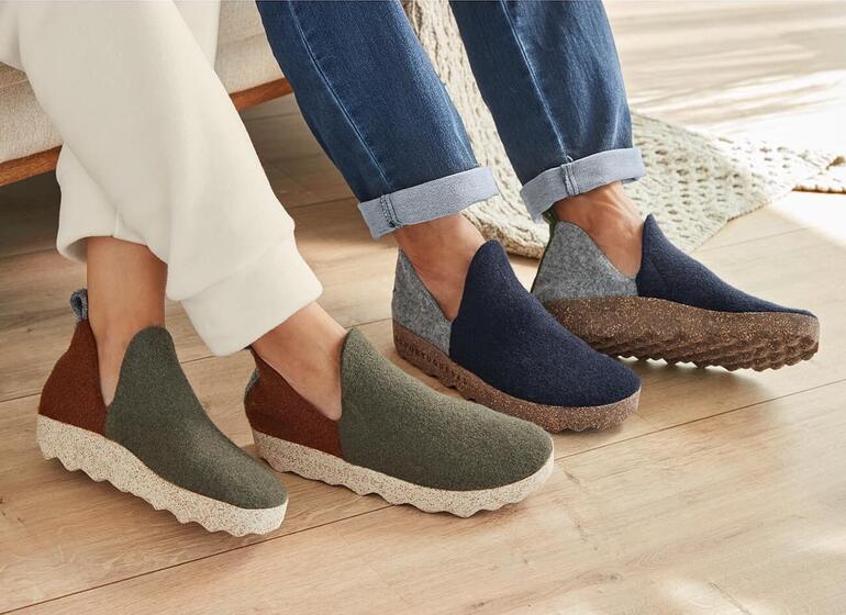 Zwei Paare Sneaker-Hausschuhe in verschiedenen Farben nebeneinander auf dem Boden.
