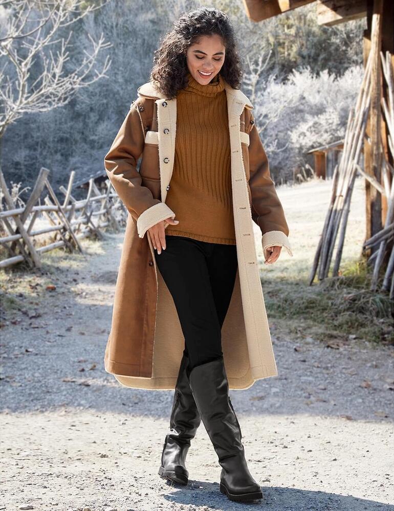 Casanova Lammfell-Stiefel Frau trägt lange, elegante Stiefelhose, kombiniert mit einem langen Mantel.