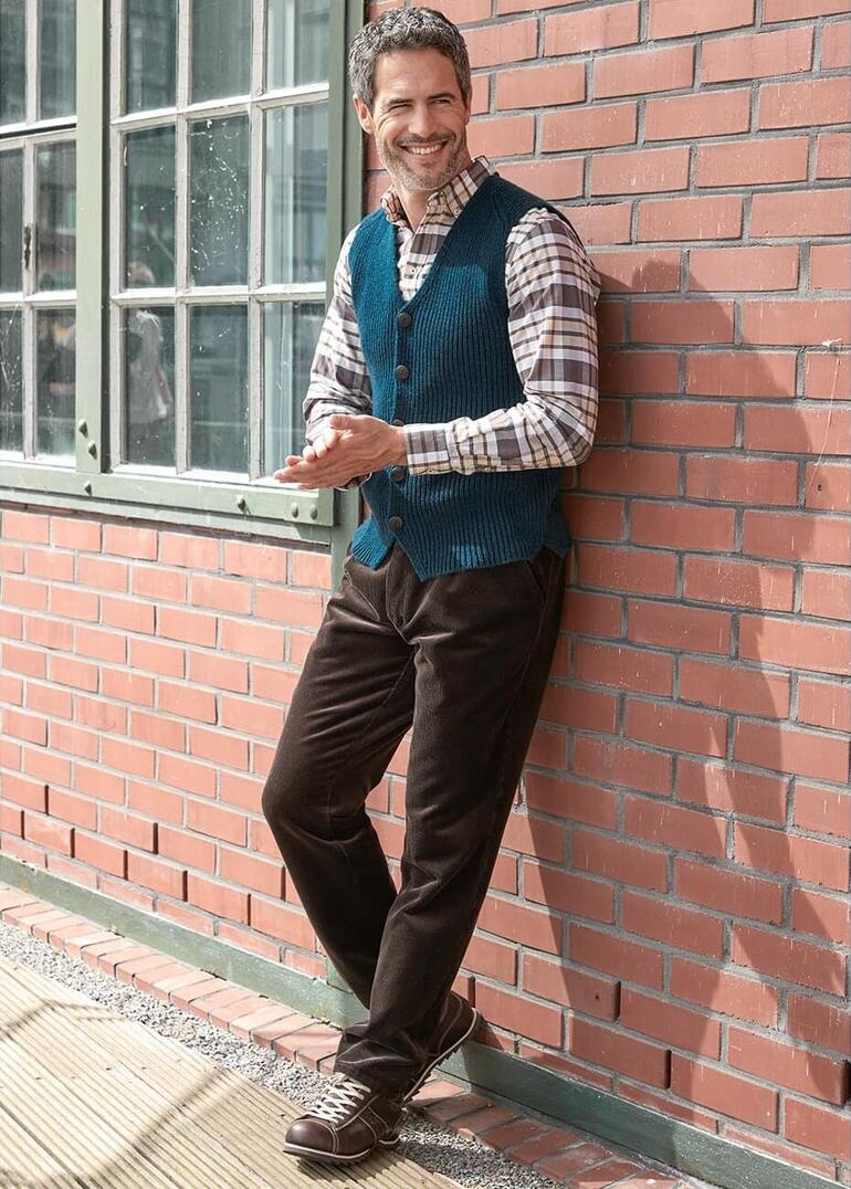 Petrol Mann in blauer Weste mit kariertem Hemd an Ziegelwand.