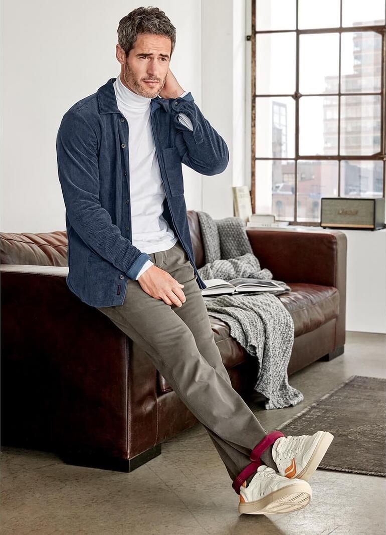 Mann sitzt auf einem Sofa in einem Jersey-Cordhemd, Seitansicht.